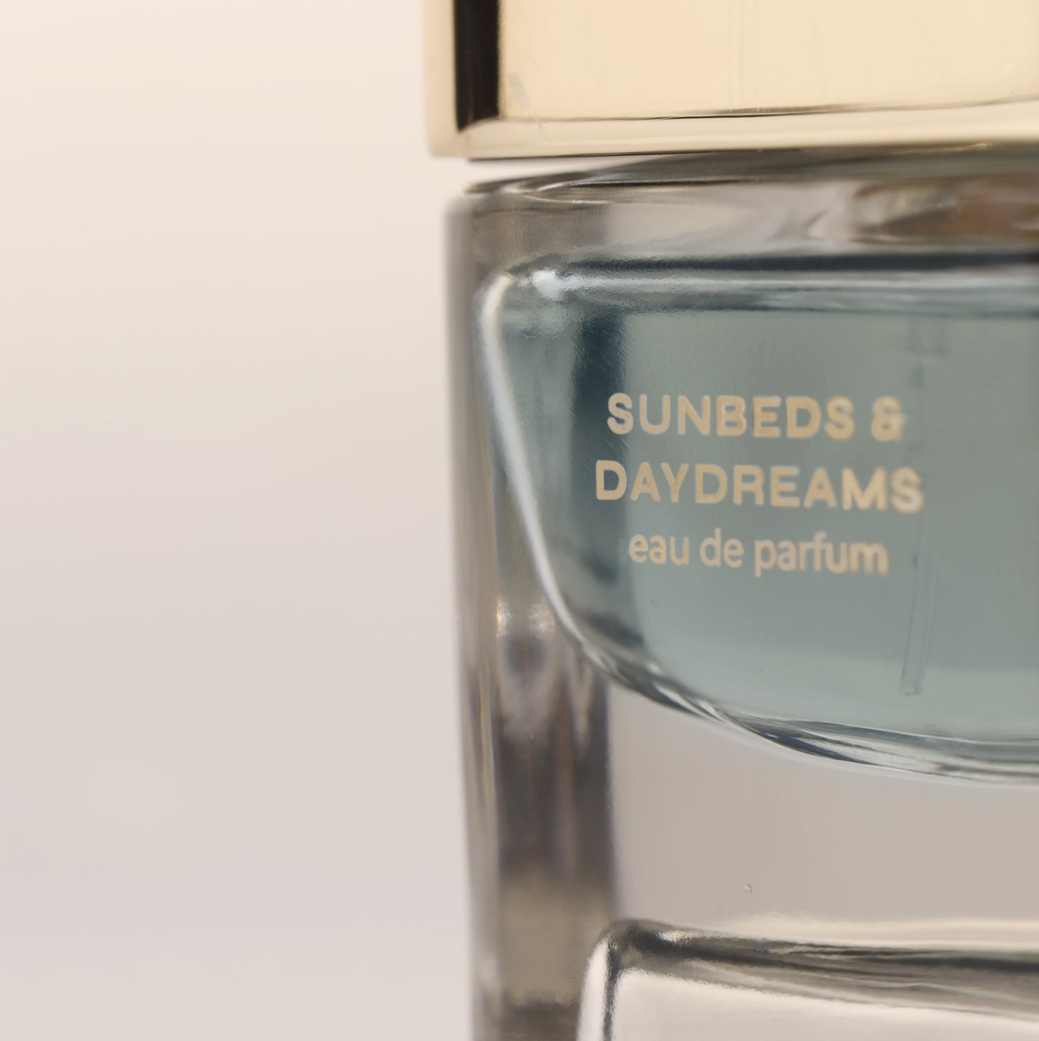 Close-up of Sunbeds & Daydreams eau de parfum bottle with golden cap and turqouise fragrance liquid, luxury niche perfume for men and women.