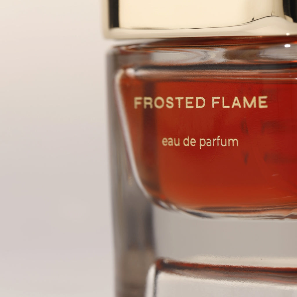 Close-up of Frosted Flame eau de parfum bottle with golden cap and amber fragrance liquid, luxury niche perfume for men and women.