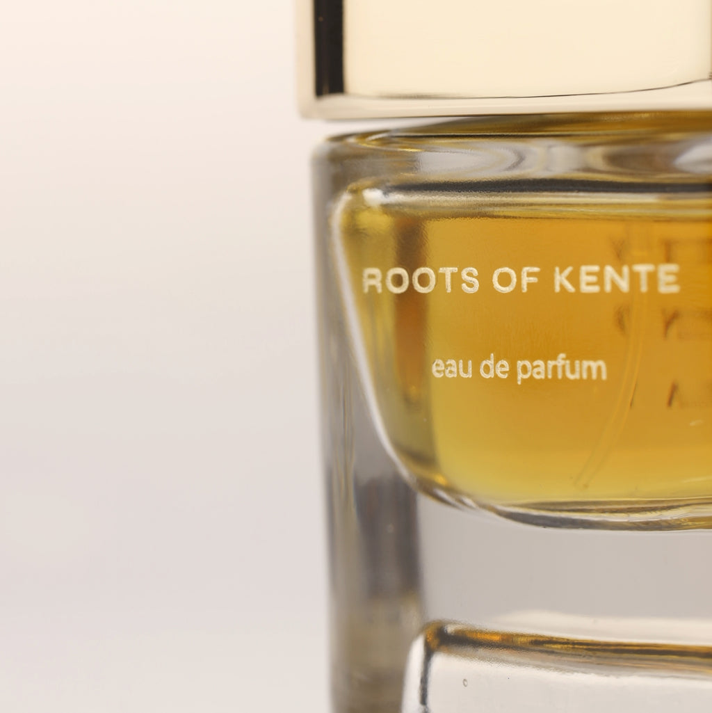 Close-up of Roots of Kente eau de parfum bottle with golden cap and golden fragrance liquid, luxury niche perfume for men and women.